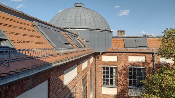 Gebäude. Dach mit Dachfenstern mit Jalousien verschlossen. Eine graue Kuppel.